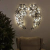 Carved metal wall decor featuring angel wings design, illuminated with soft light, perfect for home decoration.
